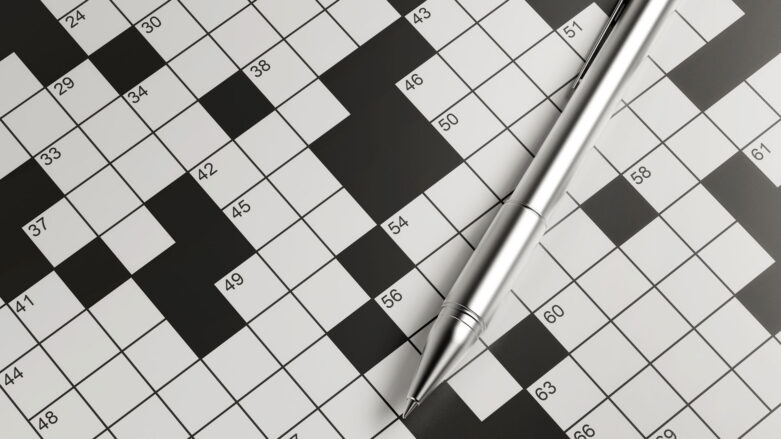 Paper crossword puzzle with a silver pen laying on top of it.